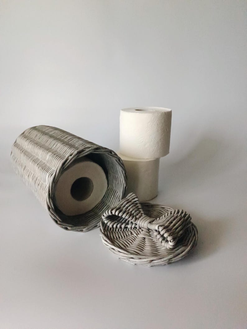 Gray toilet paper holder basket lying sideways next to two toilet paper rolls and a detached lid. Highlighting texture and size