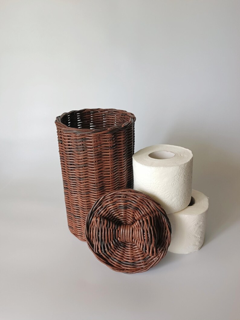 Brown toilet paper storage basket with a close-up of the lid featuring a woven bow; two rolls beside for reference. Cozy and unique bathroom piece.