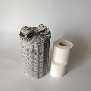 Gray paper wicker toilet roll box standing upright next to two paper rolls. Simple and elegant organization.
