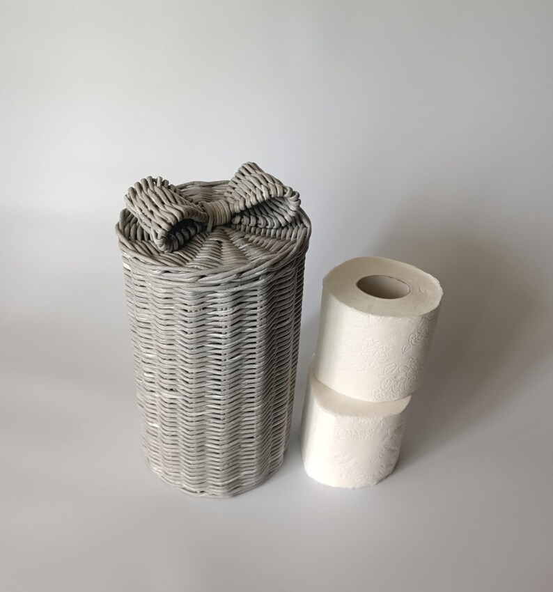 Gray paper wicker toilet roll box standing upright next to two paper rolls. Simple and elegant organization.