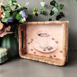 May include: A rectangular woven tray with a coffee-themed design. The tray features a watercolor illustration of a coffee cup and scattered coffee beans. The tray is made of light brown woven material and is suitable for serving.