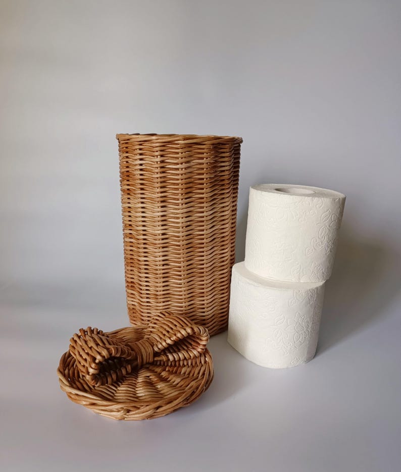 Natural color wicker toilet paper basket next to two stacked rolls, showing its internal capacity. Compact and charming storage