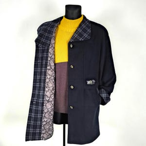 May include: A navy blue coat with a plaid lining and a small logo on the left side. The coat has a button closure and a collar. The coat is being worn over a yellow turtleneck sweater and a brown sweater.