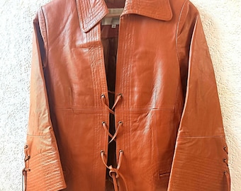May include: A brown leather jacket with a lace-up front and long sleeves. The jacket has a collar and a pocket on the left side.