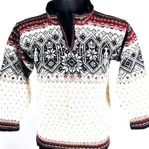 Puede incluir: Un suéter color crema con un patrón geométrico en negro, blanco y burdeos. El suéter tiene un cuello alto con cremallera parcial y está adornado con un diseño detallado de copo de nieve. Las mangas y el dobladillo presentan un borde estampado.