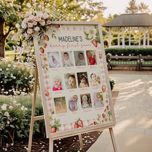 Puede incluir: Un expositor de fotos enmarcado sobre un caballete, con una cuadrícula de doce fotos de bebé. El expositor está decorado con motivos de fresas y flores, y el texto "MADELINE'S berry first year" está en la parte superior. Las fotos están numeradas.