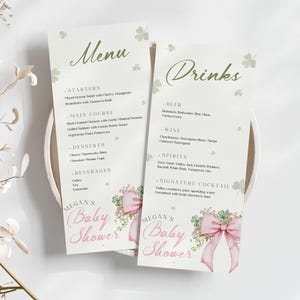 May include: Two baby shower menu cards with the words "Menu" and "Drinks" in green script. The cards have a light background with shamrock and floral accents. The words "Megan's Baby Shower" are printed in pink.