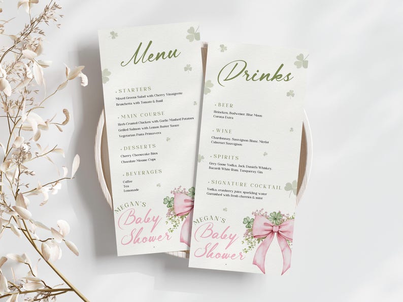 May include: Two baby shower menu cards with the words "Menu" and "Drinks" in green script. The cards have a light background with shamrock and floral accents. The words "Megan's Baby Shower" are printed in pink.
