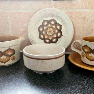 Könnte beinhalten: Ein Vintage-Set aus braunen und weißen Keramik-Teetassen und Untertassen mit geometrischem Muster. Das Set enthält eine Kanne, eine Zuckerdose und eine Teetasse mit Untertasse.