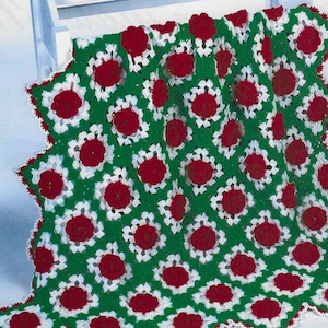 May include: A crocheted blanket with a green background and red and white flowers. The blanket has a scalloped edge.