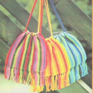 Könnte beinhalten: Drei gehäkelte Taschen mit gestreiften Mustern in Rosa, Gelb und Blau mit langen Fransen als Quasten, die an einem Holzgeländer hängen.
