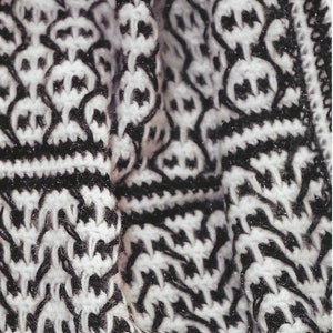 May include: Close-up of a black and white knitted fabric with a geometric pattern. The fabric is soft and textured, with a repeating design of interlocking shapes.
