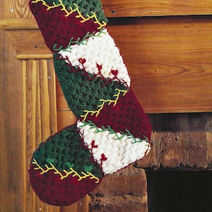 May include: A crocheted Christmas stocking with a patchwork design in green, red, and white. The stocking is hanging on a wooden mantel.