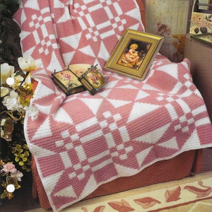 May include: A pink and white crocheted throw blanket with a geometric pattern. The blanket is draped over a chair with a floral patterned rug underneath.