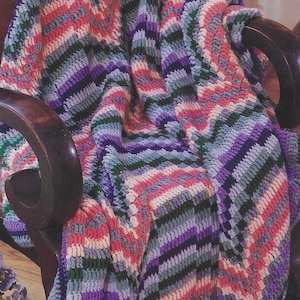 May include: A striped crocheted blanket in shades of pink, purple, green, and blue. The blanket is draped over a wooden armchair.
