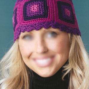 May include: A crocheted hat in shades of purple and pink. The hat features a square pattern design with a scalloped edge. The hat is handmade and appears to be a winter accessory.