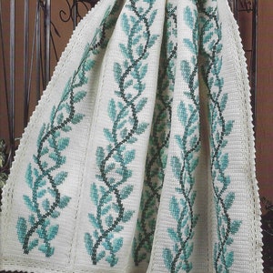 Puede incluir: Una manta de ganchillo blanca con un patrón de enredadera de hojas verdes. La manta tiene un borde de ganchillo.