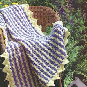 May include: A crocheted blanket with a purple and yellow striped pattern. The blanket has a scalloped edge and is draped over a wicker chair.