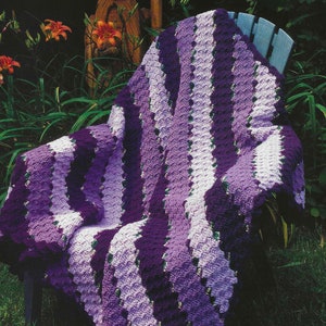 May include: A purple and white crocheted throw blanket draped over a wooden chair in a garden setting.