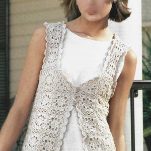 Op de afbeelding: Een crèmekleurig, mouwloos gehaakt vest met een geschulpte rand. Het vest heeft een bloemenpatroon en is aan de voorkant dichtgeknoopt. Het kledingstuk wordt over een witte top gedragen.