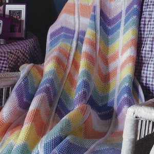 Puede incluir: Una manta de crochet con chevron arcoíris con fondo blanco. La manta está hecha con una variedad de colores, incluyendo morado, azul, verde, amarillo y naranja.