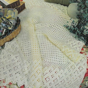 May include: A white crocheted throw blanket with a lacy edge. The blanket is folded in half and draped over a bed.