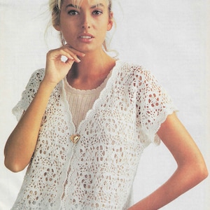 May include: A white crocheted cardigan with a heart-shaped button. The cardigan has a V-neck and short sleeves.