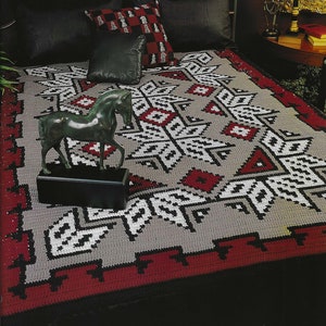 Peut inclure: Une couverture en crochet grise et rouge avec un motif géométrique. Une sculpture de cheval en bronze est placée sur la couverture.