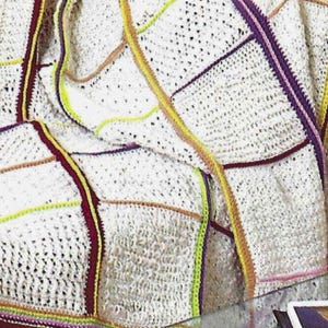 May include: A white crocheted blanket with colorful stripes. The blanket is made of a soft, textured yarn and has a patchwork design.