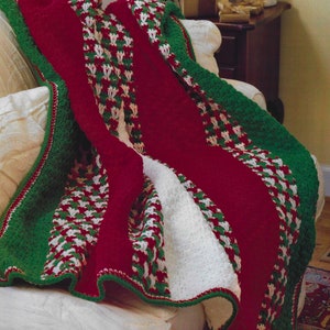May include: A red, green, and white crocheted throw blanket with a white fleece lining. The blanket is draped over a white armchair.