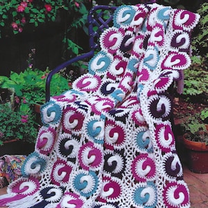 May include: A crocheted throw blanket with a swirling pattern in shades of pink, teal, white, and black. The blanket has a fringe border and is draped over a blue metal chair.