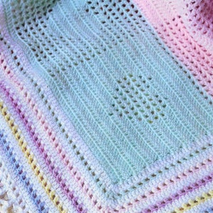 May include: A crocheted baby blanket with a pastel rainbow border and a light blue centre. The blanket is made with a delicate open stitch pattern.