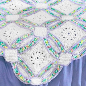 以下が含まれることがあります： 手作りの白いかぎ針編みの毛布で、花の模様が施されています。毛布は、正方形と円の繰り返し模様で、ラベンダーとマルチカラーの糸で繋がれています。毛布は柔らかく居心地が良く、ベッドやソファに最適です。