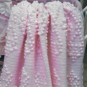 May include: A pink and white crocheted baby blanket with a textured, bobble stitch pattern.