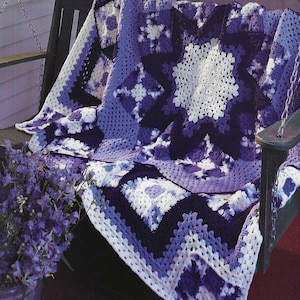 May include: A crocheted blanket with a star pattern in shades of purple, blue, and white. The blanket is draped over a wooden chair on a porch.