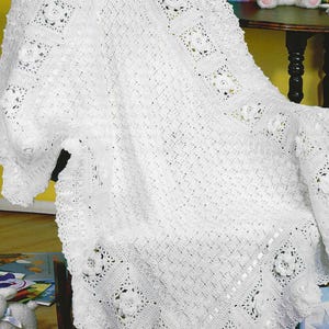 Puede incluir: Una manta blanca de ganchillo con un patrón floral. La manta está sobre una silla, mostrando su intrincado diseño. Los detalles florales son prominentes, agregando un toque delicado. La textura y el diseño sugieren un artículo hecho a mano.