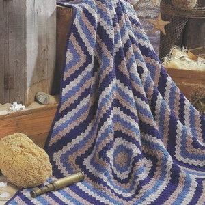 May include: A blue, gray, and white crocheted blanket with a geometric pattern. The blanket is folded and draped over a wooden crate.