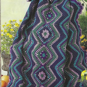 May include: A crocheted blanket with a geometric pattern in shades of purple, teal, and green. The blanket is made with a variety of stitches and has a scalloped edge.