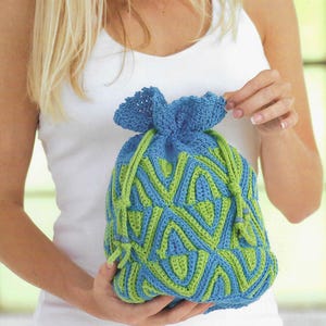Peut inclure: Un sac à cordon en crochet bleu et vert avec un motif géométrique. Le sac est tenu par une personne portant un débardeur blanc. Le cordon du sac est vert.