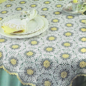 May include: White crochet tablecloth with a yellow and green floral pattern. The tablecloth has a scalloped edge and is laid on a teal table.