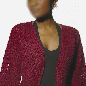 May include: A burgundy crochet bolero with long sleeves. The open-front cardigan features a delicate, openwork stitch pattern. The garment is worn over a black top, creating a contrast in color and texture. The bolero is a stylish layering piece.