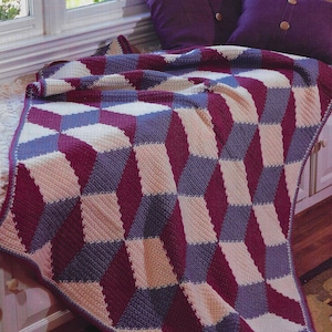 Könnte beinhalten: Eine gehäkelte Tagesdecke mit einem geometrischen Muster in den Farben Lila, Creme und Burgunderrot. Die Decke ist gefaltet und über einem Fenstersims gelegt.