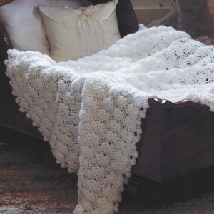 May include: A white crocheted baby blanket with a delicate pattern, draped over a wooden cot with a white pillow.