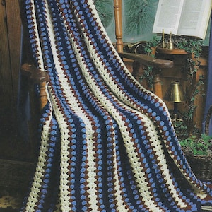 Puede incluir: Una manta de ganchillo con rayas azules, blancas y marrones. La manta está colocada sobre una mecedora de madera. El texto "Hooked on Crochet! 7 Best Afghans" es visible en la esquina inferior izquierda de la imagen.