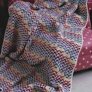 May include: A multi-colored crocheted blanket with a chevron pattern in shades of purple, red, green, and cream. The blanket is draped over a chair with a red fabric.