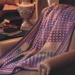 Puede incluir: Una manta de ganchillo multicolor con un patrón texturizado. La manta está drapeada sobre un sillón de cuero marrón.