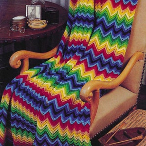 Könnte beinhalten: Eine bunte Häkeldecke mit einem Zickzackmuster in Rot-, Orange-, Gelb-, Grün-, Blau- und Violetttönen. Die Decke liegt über einem Holzsessel.