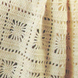 Könnte beinhalten: Nahaufnahme einer cremefarbenen Häkeldecke. Die Decke weist ein sich wiederholendes Muster aus floralen Designs und Durchbrucharbeiten auf, wodurch eine strukturierte Oberfläche entsteht. Die weiche, cremefarbene Farbe und die aufwendigen Stiche deuten auf einen handgefertigten Artikel hin.