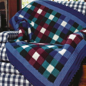 May include: A blue, green, white, and burgundy crocheted throw blanket with a checkered pattern. The blanket is draped over a blue and white checkered armchair.