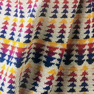 Könnte beinhalten: Eine bunte gehäkelte Decke mit einem geometrischen Muster aus Dreiecken in Rot-, Gelb-, Blau- und Weißtönen.